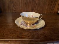 Gold hand-painted teacup and floral saucer on wood surface.