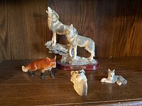 Photo showing the group of wolf and fox figurines including two wolves on a pedestal, a fox figure, reclining wolf, small wolf head hanger, and small resting wolf cub.