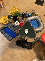 Full lot view showing multiple camping gear items including inflatable seat, thermoses, camping chair, cooking pots, sit pads, and storage bags on carpeted floor.