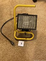Front view of flood work light showing yellow metal frame, glass cover, and electrical plug