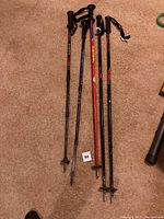 Photo showing two adjustable hiking poles laid on carpet floor, black handles with wrist straps visible, red and black shafts.