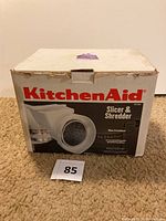 Box labeled KitchenAid Slicer and Shredder showing front and branding. Box shows minor wear consistent with used condition.