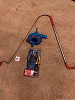 Full view of the plumbing auger, strap wrench packaging, and another tool together on carpeted floor.