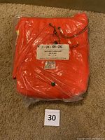 Folded bright orange safety jacket in plastic packaging with label showing size 2XL and style info.