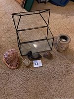Glass display box with black metal frame open, large conch shell, smaller seashells, bird figurines, candle holder.