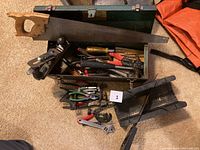 Photo showing green metal toolbox filled with assorted hand tools including saw, screwdrivers, pliers, clamps, and wrench.