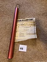 Red metal tube, instruction sheet, and small parts for Trailblazer Collapsing Saw on carpeted floor