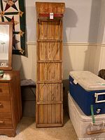 Full view of the wooden toboggan standing upright showing its length, construction, and shape.