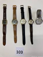 Front view of five wristwatches laid flat in a row showing various dial designs and strap types.