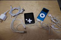 Two MP3 players, charging cables, earbuds, and chargers displayed on a wooden surface.