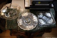 Photo showing all three depression glass dishes with silver overlay floral designs placed on a dark green marble surface.