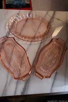 Top-down view of three pink depression glass serving dishes on marble surface: one oval platter embossed with poinsettia flowers and two smaller rectangular dishes with starburst patterns.