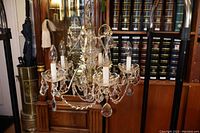 5 light chandelier with crystals and bulbs hanging, shown in front of wood cabinetry with shelves and books.