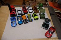 Full view of all 13 toy cars and one small dinosaur/dragon toy, arranged on a surface
