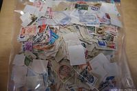 Photo of a large clear plastic bag filled with loose postage stamps of various colors and designs including red, purple, blue, and green.