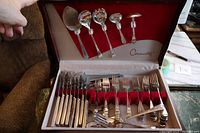Opened lined case showing multiple forks, knives and serving utensils arranged in red velvet slots.
