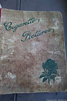 Worn cigarette card album cover with green text and rose illustration