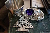 Wide view of all silver plated lot items showing ice bucket, Christmas tree trivet, small bowl with blue cobalt liner, handled tray, and gravy boat.