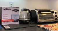 Photo showing Aroma electric kettle with its box and Black and Decker toaster oven on countertop.