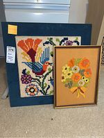 Two framed hook rug style art pieces shown side by side on carpeted floor in front of a stove