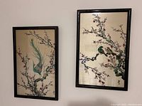 Two framed Asian style bird pictures hanging on wall, showing birds and blossoms on silk-like background in black bamboo style frames.