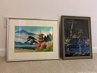 Two framed Asian style art prints leaning against a wall, showing the overall lot arrangement and framing.