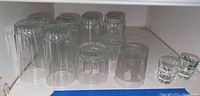 View of clear glass drinking glasses and shot glasses arranged in a white shelf.