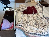 Overview image showing bedding spread on mattress and folded clothing inside wooden bench next to bed.