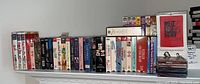 Wide view of DVDs, CDs, and VHS tapes arranged on shelf, showing multiple titles including musicals and workout videos
