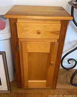 Front view of the wooden cabinet with drawer and door, showing the knobs and wood grain.