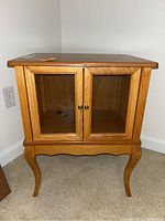 Front view of a wooden cabinet with two glass front doors and decorative curved legs.