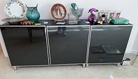 Front view of the cabinet showing three reflective black doors with various items placed on top (not included).