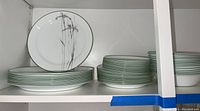 Multiple Corelle plates stacked on shelves, showing dinner plates, salad plates, and bread and butter plates all matching with green rims and floral design.