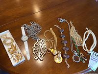 Overview of several costume jewelry items on a table including necklaces, pins, and watch