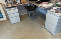 Both metal filing cabinets positioned under a desk in an office environment, showing overall condition and size relative to surroundings.