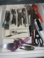 Photo of the flatware and kitchen tools arranged in a drawer organizer tray showing various spoons, forks, knives, and other utensils including shears and scoop