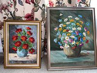 Two framed floral paintings. One with red flowers in a blue vase, other with mixed flowers in a brown pot.