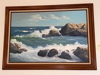 Full frontal view of the framed painting showing ocean waves crashing on coastal rocks with some birds and cloudy sky visible.