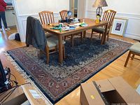 Full view of a hand-knotted Oriental rug under a dining table showing overall pattern and intact fringe