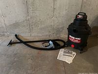 Full kit showing Shop-Vac vacuum, hose, attachments, and instruction manuals against concrete wall and floor.