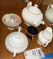 Porcelain tea set with teapot, sugar bowl, creamer, floral cup, dark blue cup and white cup with gold trim and wavy embossed design
