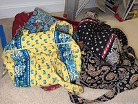 Three cloth bags arranged side by side on the floor. One yellow/blue Vera Bradley bag, one black/red Vera Bradley bag, and one large red unlabeled cloth bag.