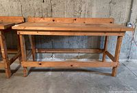 Front view of a large wooden work bench against concrete wall, showing sturdy frame and upboard back support.