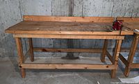 Full front view of wooden workbench with attached red Arrow brand vice on right corner.