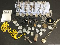 Overview of rosaries arranged on a white display stand with various religious pendants spread out on black surface.