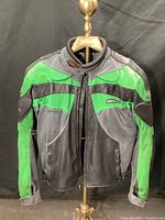 Front view of green, black, and gray Fieldsheer motorcycle jacket showing details of textile and mesh materials, shoulder and elbow protection, zippered pockets, and front zipper closure.