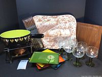 Full set of fondue items including pot, burner, forks, lacquerware plates, wine glasses, wooden tray, and large swan platter all shown grouped