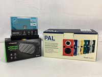 Three boxed speakers: Tivoli PAL in largest box, Altec Lansing Mini H2O in small case on top left, Polaroid wireless speaker in black box bottom left.