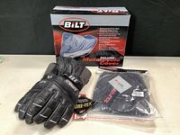 Scott Gore-Tex black gloves size large with tags, Bilt motorcycle cover box in background, and sealed package of Tourmaster boot rain covers