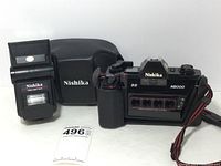 Photo of Nishika N8000 camera, black protective carrying case with 'Nishika' logo, and Nishika Twin Light 3010 flash unit on white surface.